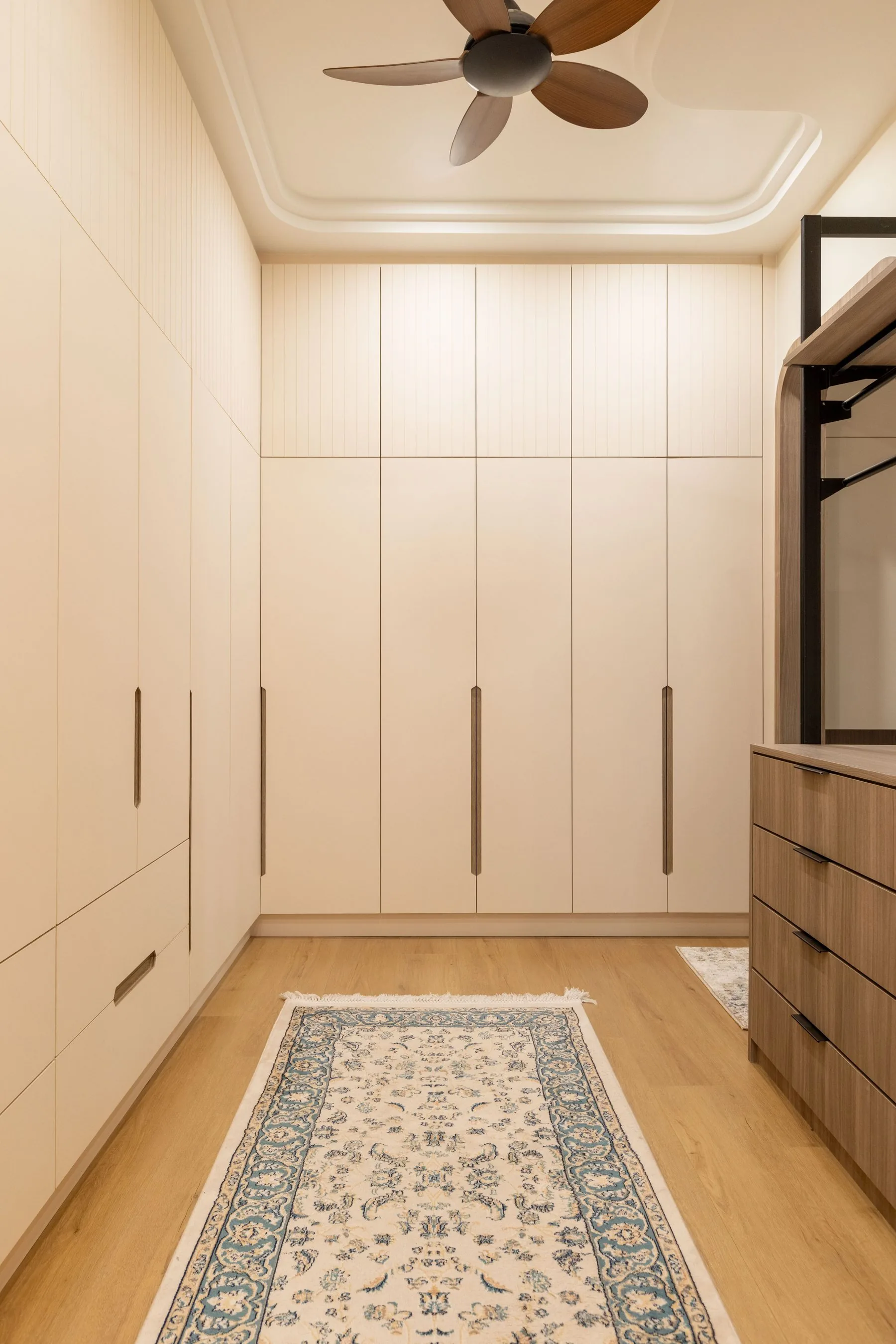 Walk-in wardrobe corridor lined with cream cabinetry and drawers — Cabinet Studio